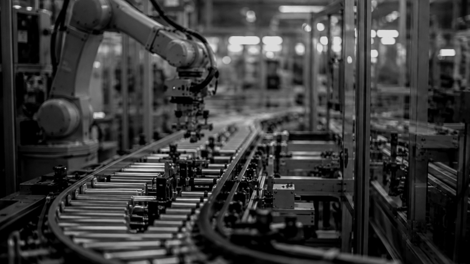 A production hall, a robotic arm over a conveyor, shot in grayscale
